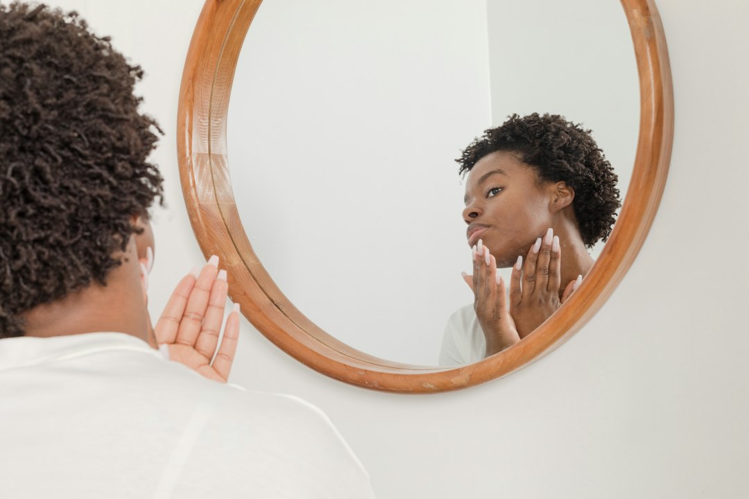 A woman examines and touches the skin on her face while looking in a mirror.